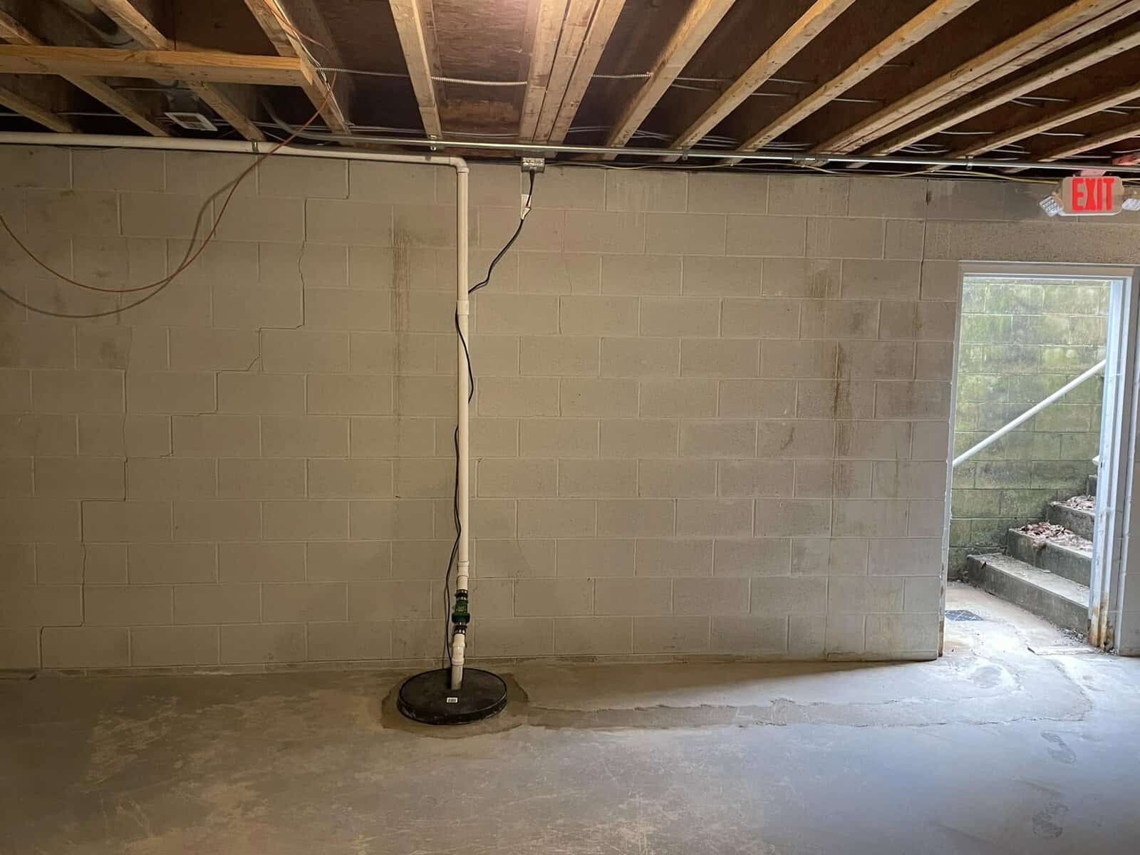 Unfinished basement with a sump pump and open door to outside, ready for help from Titan Plumbing & Drains.