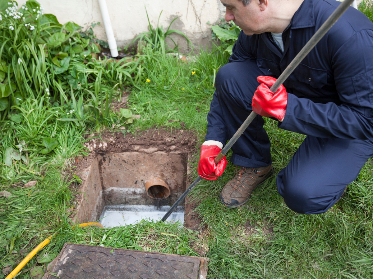 A Titan Plumbing & Drains technician is cleaning an outdoor drain to help prevent clogs and flooding.