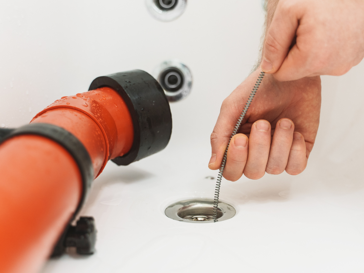 Alt: Someone from Titan Plumbing & Drains cleans a bathtub drain using a plumbing snake.