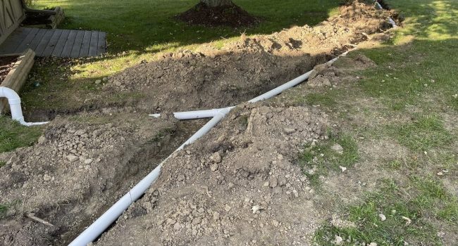 A Titan Plumbing & Drains technician is installing drainage pipes in a yard to improve water flow.